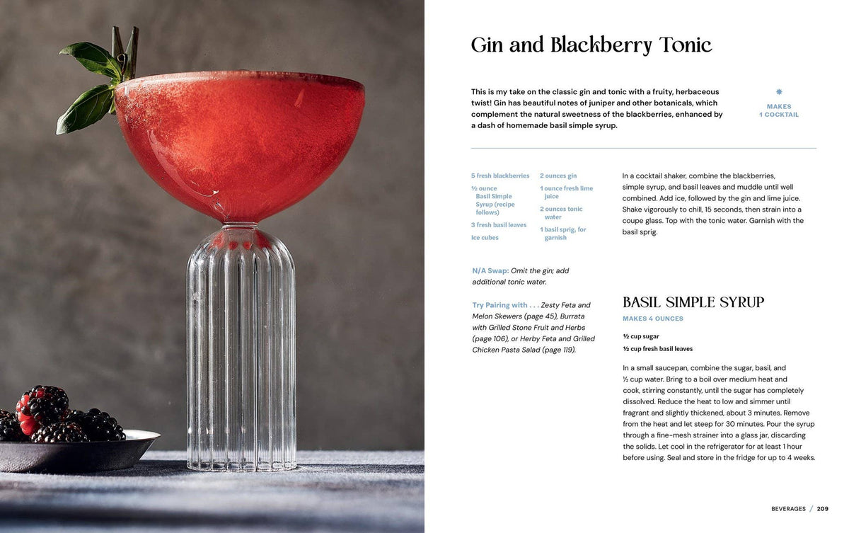 Red cocktail in a glass with basil leaves, accompanied by blackberries on a gray background.