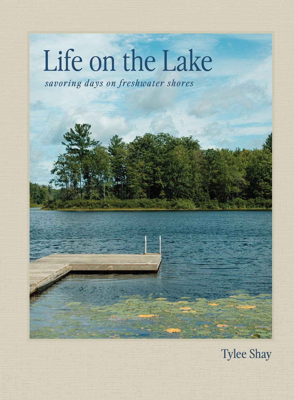 Book cover for 'Life on the Lake' by Tylee Shay, featuring a photograph of a calm lake with a wooden dock, green trees, and blue sky, set against a beige background.