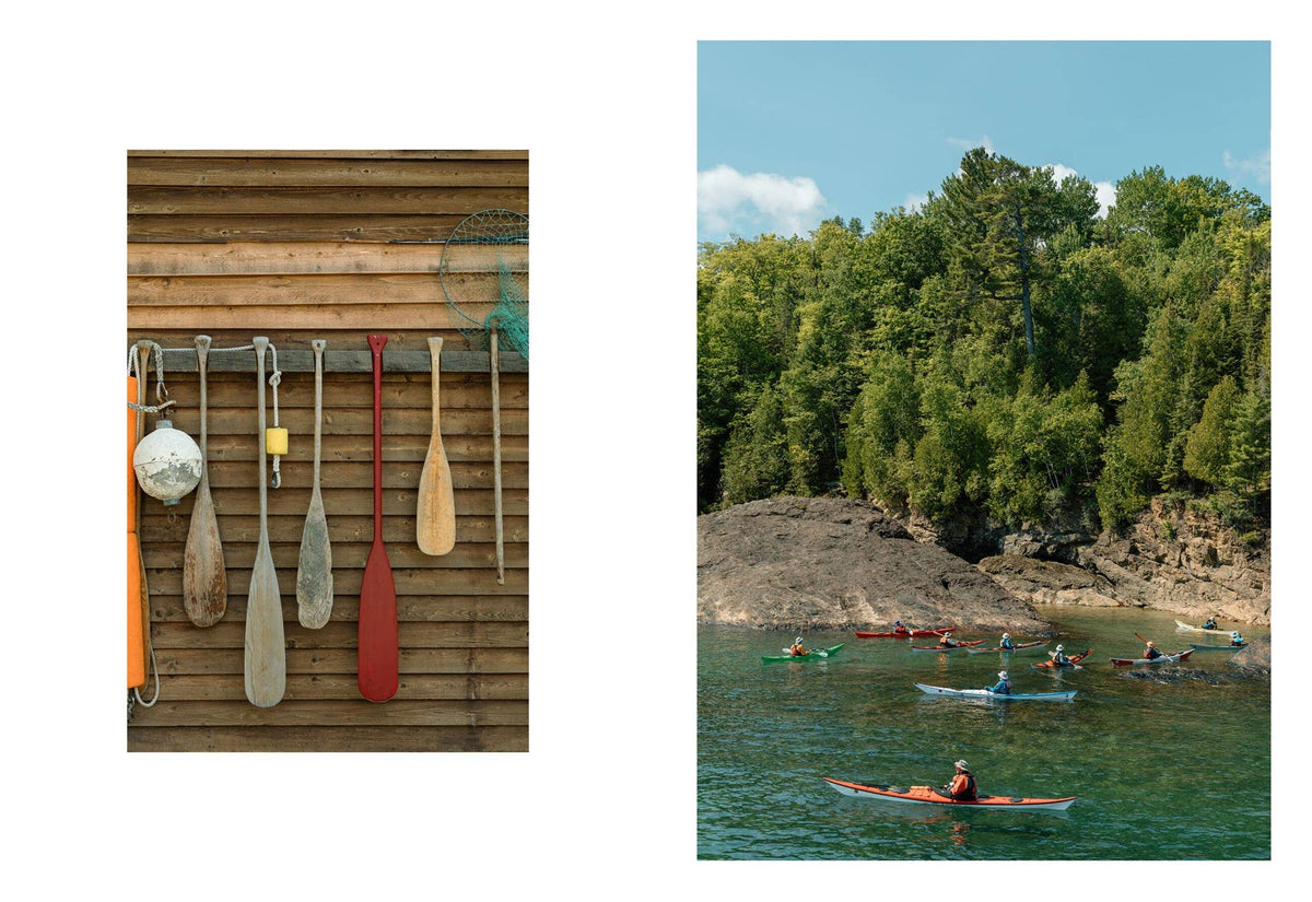 Paddles hanging on a wooden wall next to a scenic lake with kayakers.