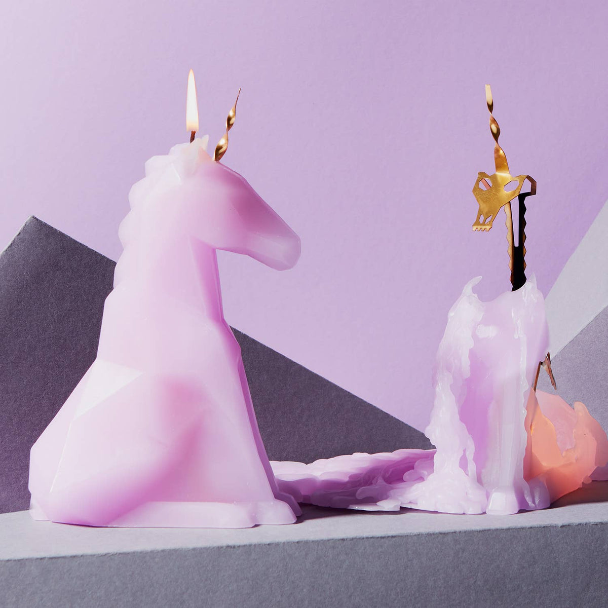 Unicorn-shaped candle with a lit wick on a purple background