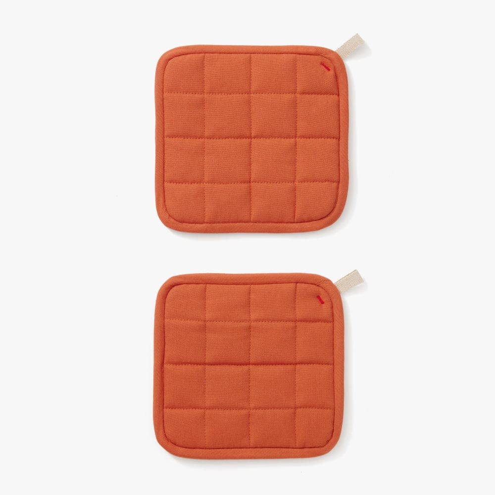 Two orange quilted pot holders on a white background