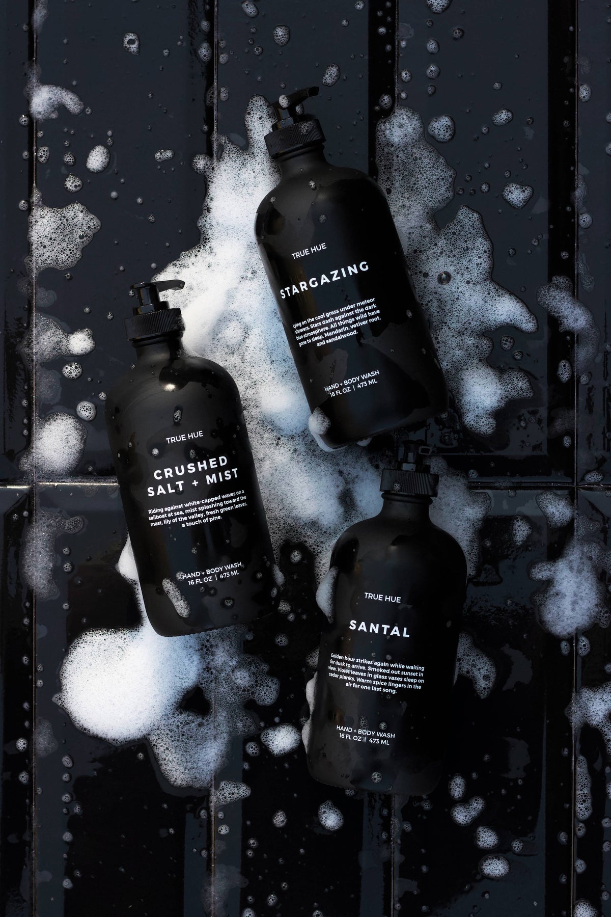 Three black bottles with labels on a textured dark surface with white foam.