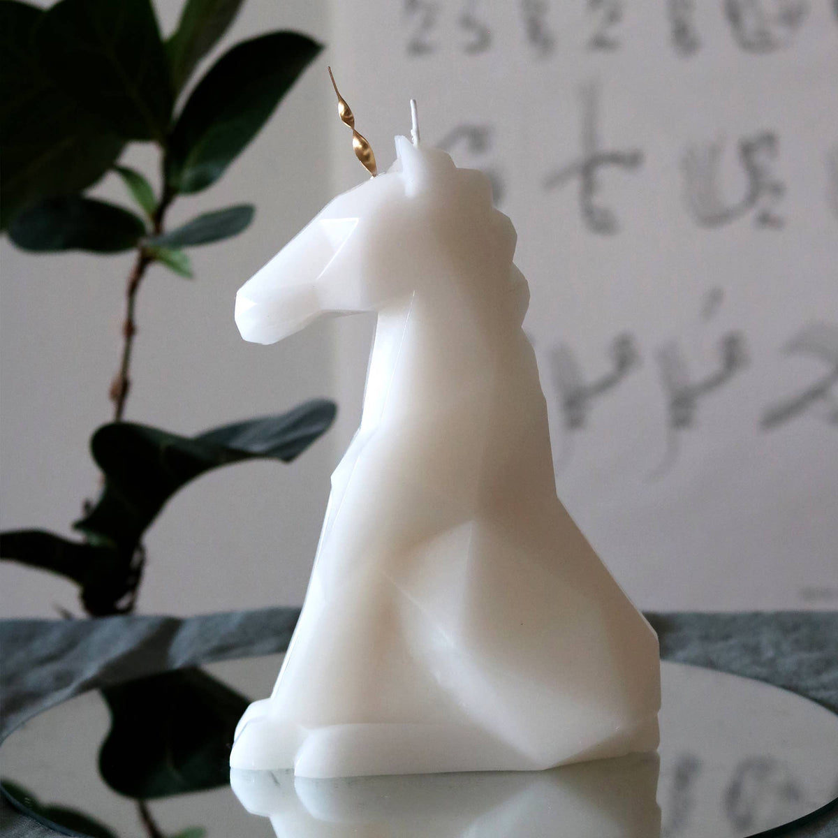 Unicorn-shaped candle on a reflective surface with a blurred background