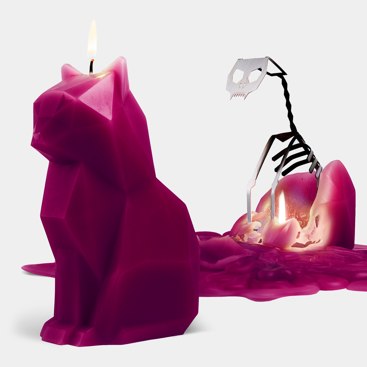 Pink cat-shaped candle melting with skeleton hand reaching towards it on a white background