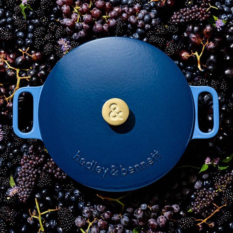 Blue cast iron cookware lid with a brand logo on a background of grapes