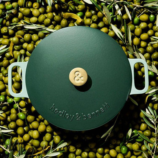 Green cast iron cookware lid with 'hedley & bennett' branding on a bed of green olives.