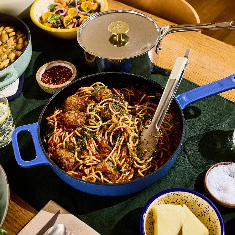 Blue skillet with spaghetti and meatballs on a dining table with side dishes.