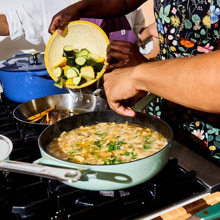 People cooking on a stove with a pan of food and a bowl of vegetables.