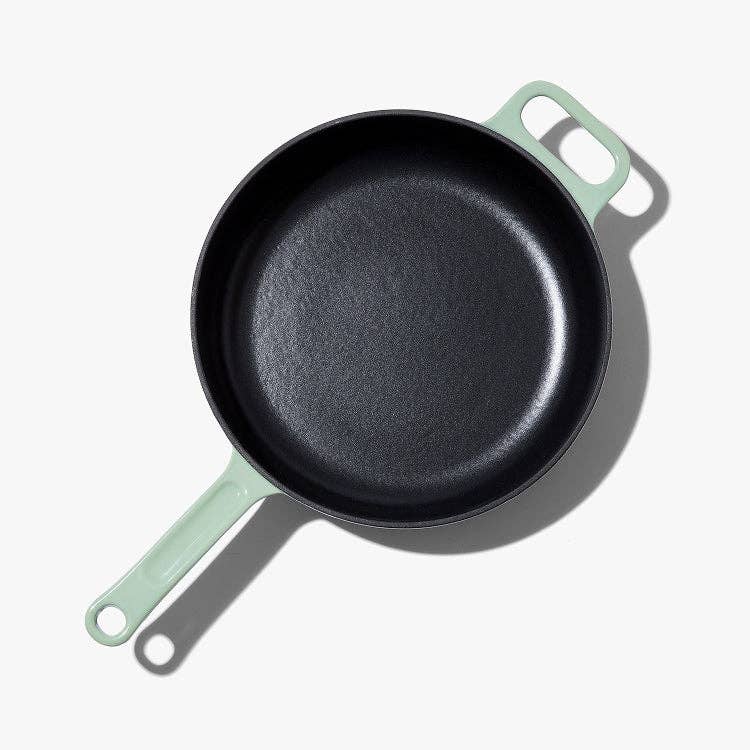 Black frying pan with light green handles on a white background