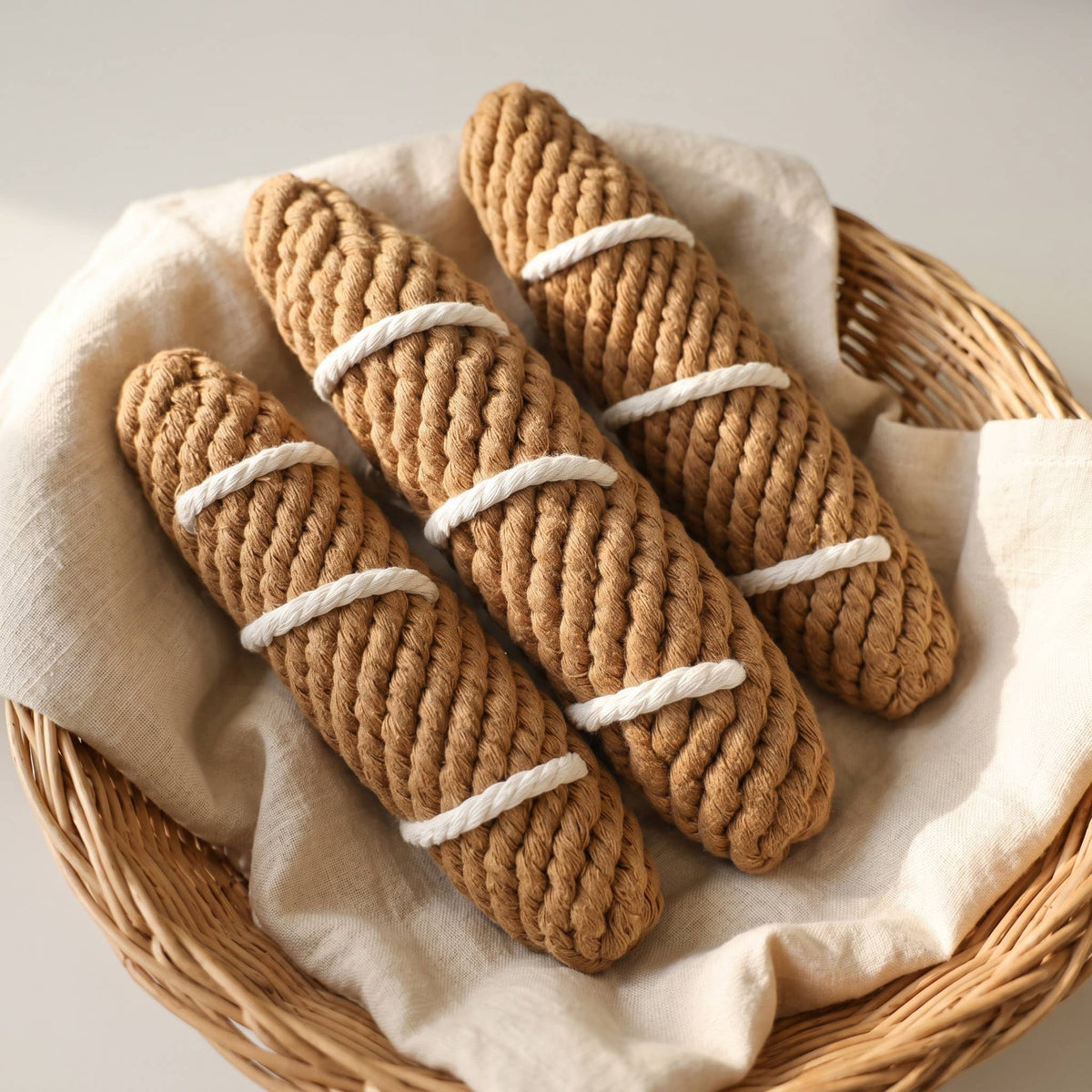 Rope toy shaped like baguettes in a basket laying on a beige linen cloth