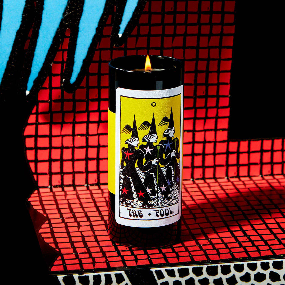 Candle with a tarot card design on a red grid background