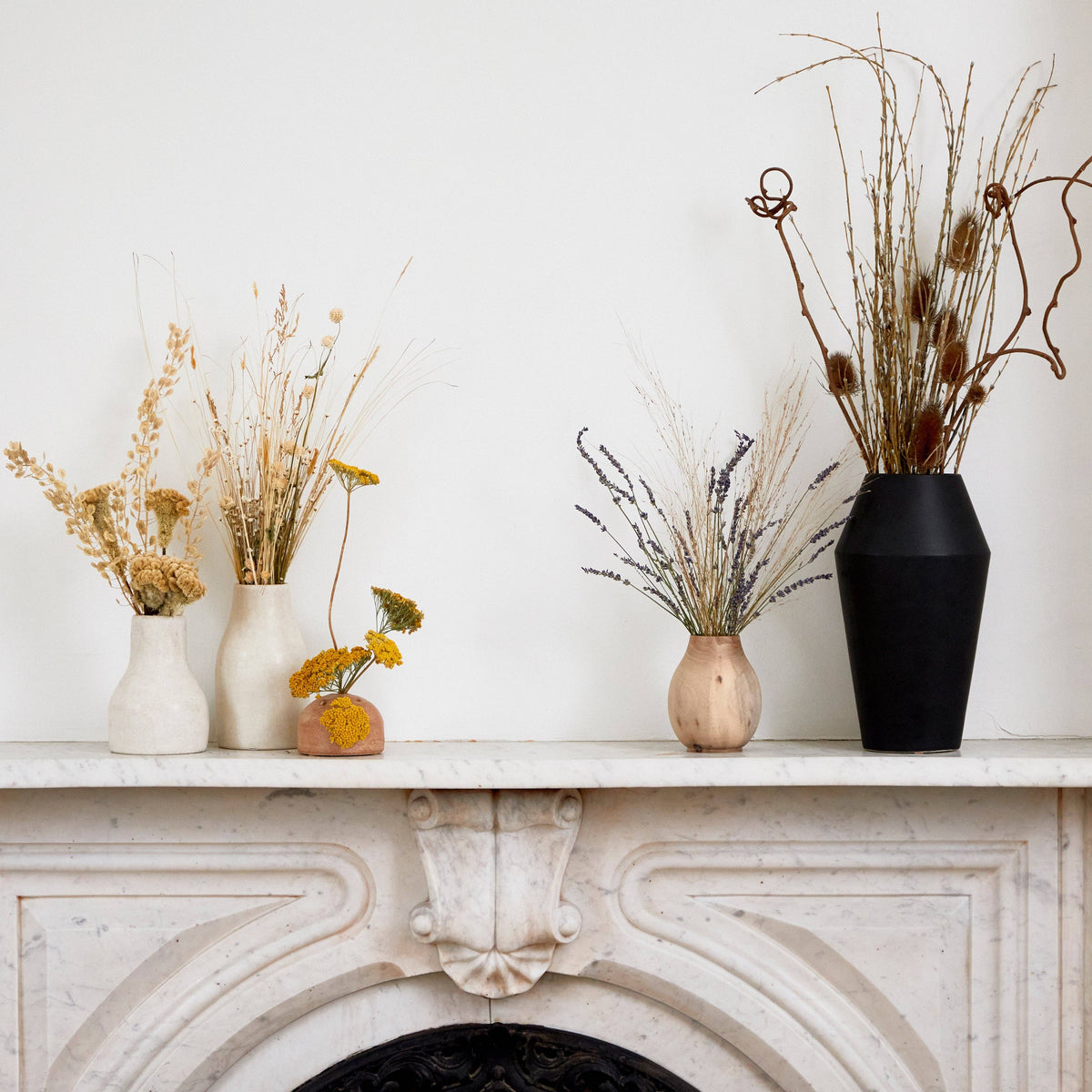 Decorative vases with dried plants on a white mantelpiece.