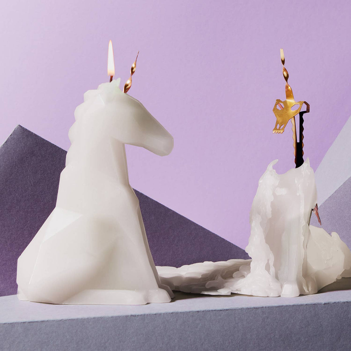 Unicorn-shaped candle with a lit flame on a purple and gray background